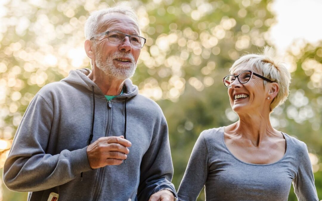 A happy, active senior couple enjoying a walk in a forest near Milton, representing the mobility and pain-free lifestyle achievable with manual osteopathy for seniors